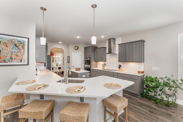 kitchen with wall chimney range hood, gray cabinetry, arched walkways, and a sink