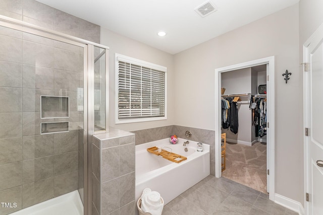 full bathroom featuring visible vents, a walk in closet, a garden tub, a stall shower, and tile patterned flooring