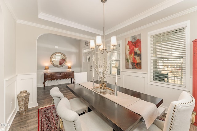 dining area with wood finished floors, an inviting chandelier, wainscoting, a decorative wall, and crown molding