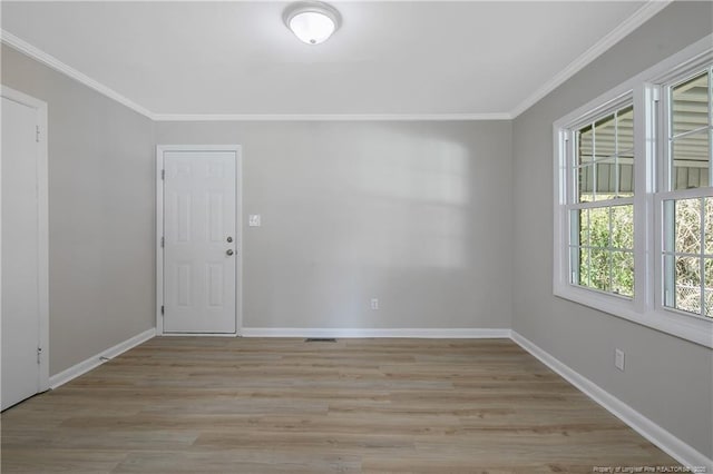 empty room featuring light wood-type flooring, crown molding, and baseboards