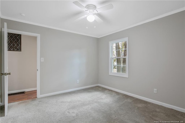 carpeted spare room featuring ceiling fan, visible vents, baseboards, and ornamental molding