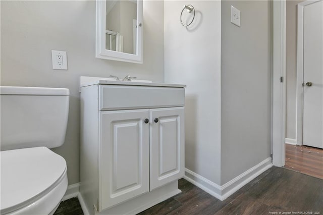 bathroom with toilet, vanity, baseboards, and wood finished floors