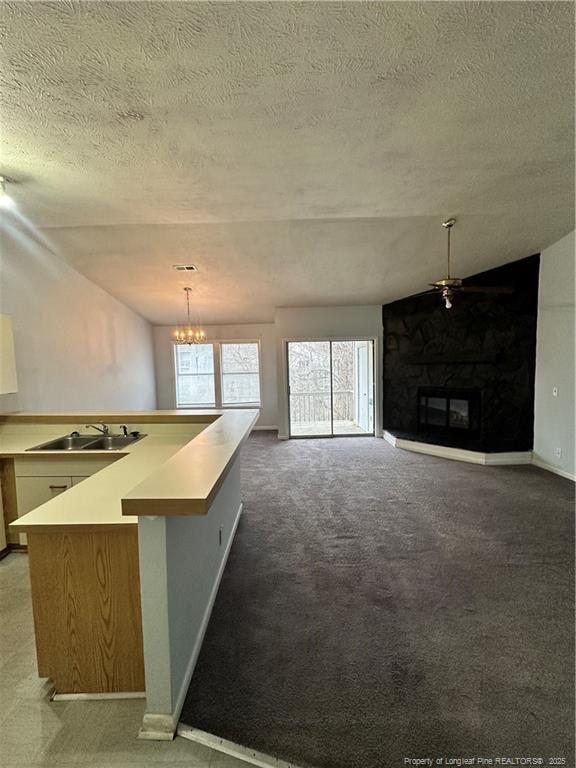 kitchen featuring a large fireplace, open floor plan, light countertops, hanging light fixtures, and a sink