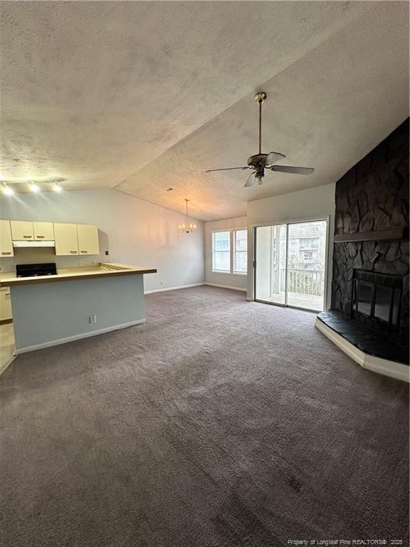 unfurnished living room with carpet, vaulted ceiling, a stone fireplace, ceiling fan with notable chandelier, and a textured ceiling