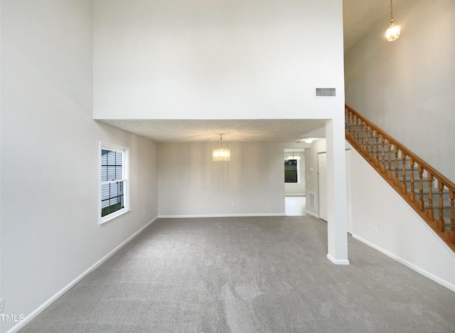 unfurnished living room with visible vents, baseboards, carpet, stairway, and a towering ceiling