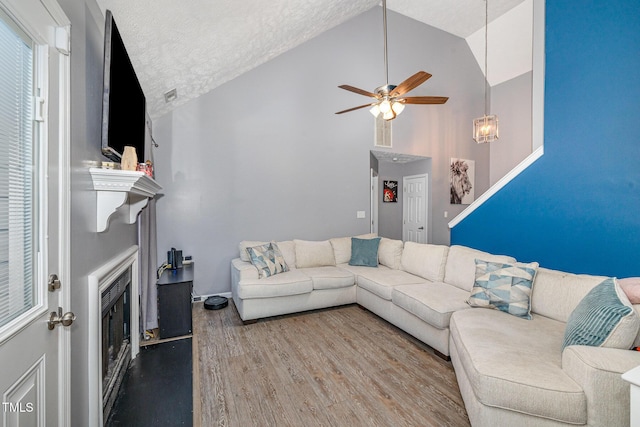 living room with high vaulted ceiling, a ceiling fan, a textured ceiling, wood finished floors, and a fireplace