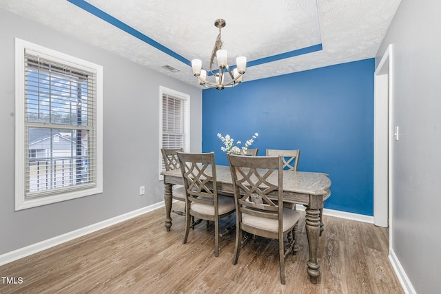 dining area with a tray ceiling, visible vents, a textured ceiling, and wood finished floors