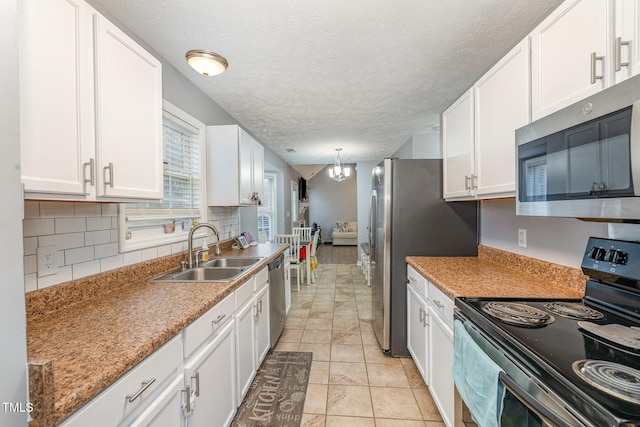 kitchen with a sink, decorative backsplash, stainless steel appliances, white cabinets, and a chandelier