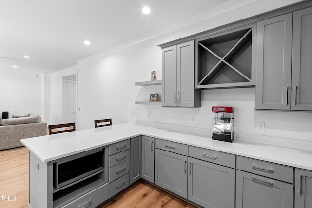 kitchen with stainless steel microwave, a peninsula, gray cabinets, and open shelves