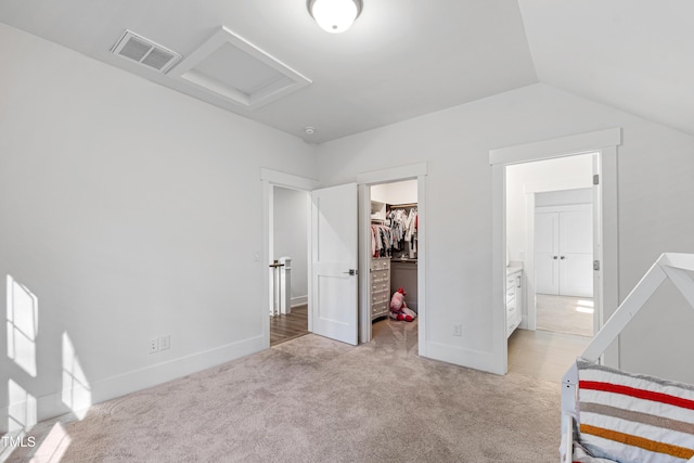 bedroom featuring visible vents, a walk in closet, lofted ceiling, light colored carpet, and attic access