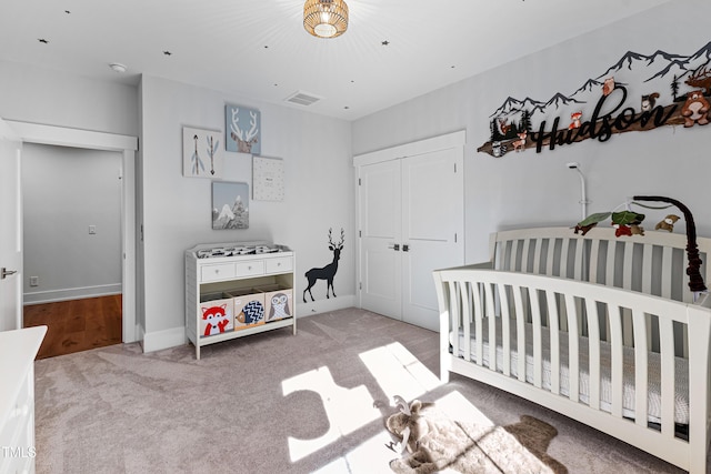 carpeted bedroom featuring visible vents, baseboards, a closet, and a crib