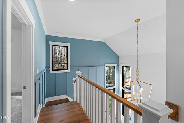 hall featuring visible vents, lofted ceiling, an upstairs landing, wainscoting, and a notable chandelier