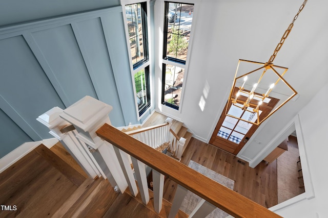 stairs featuring a decorative wall, a notable chandelier, wood finished floors, and a towering ceiling