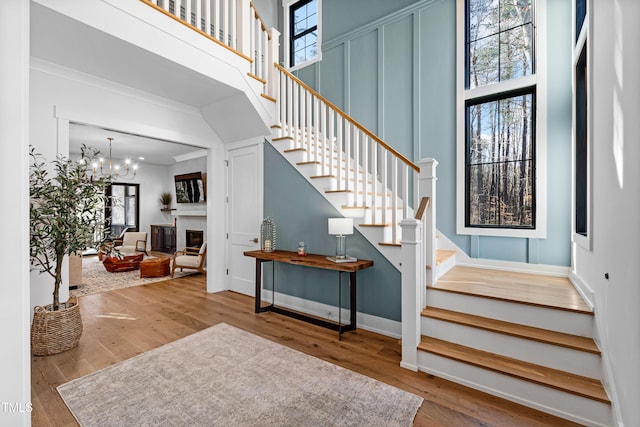 stairs with a wealth of natural light, wood finished floors, an inviting chandelier, and a towering ceiling