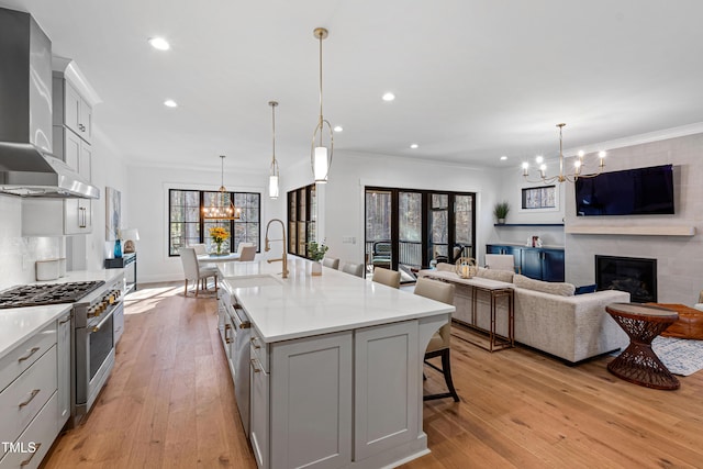 kitchen with ornamental molding, an inviting chandelier, stainless steel range, wall chimney exhaust hood, and a sink