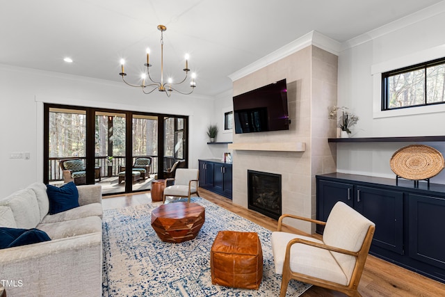 living area featuring light wood-style flooring, a tile fireplace, ornamental molding, french doors, and a notable chandelier