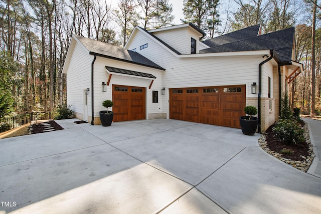 view of side of property featuring a garage, roof with shingles, and concrete driveway