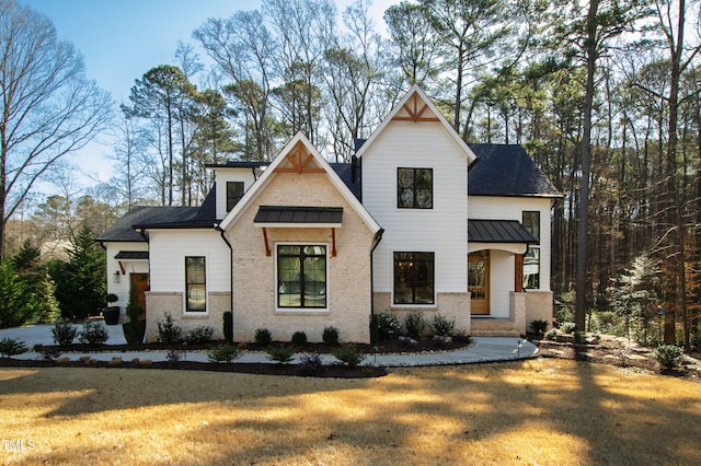 modern inspired farmhouse with brick siding, a front lawn, metal roof, and a standing seam roof