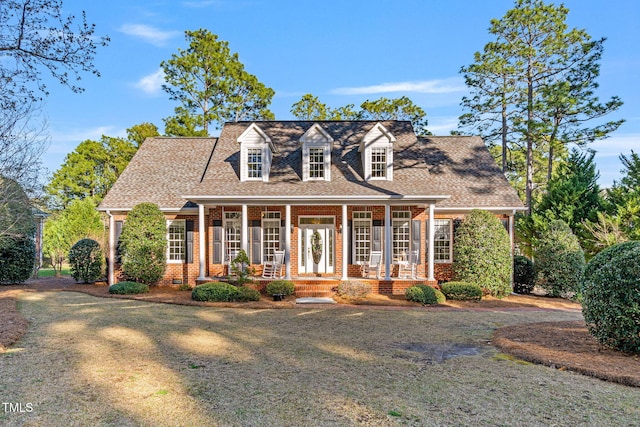 cape cod house featuring a porch, brick siding, and roof with shingles