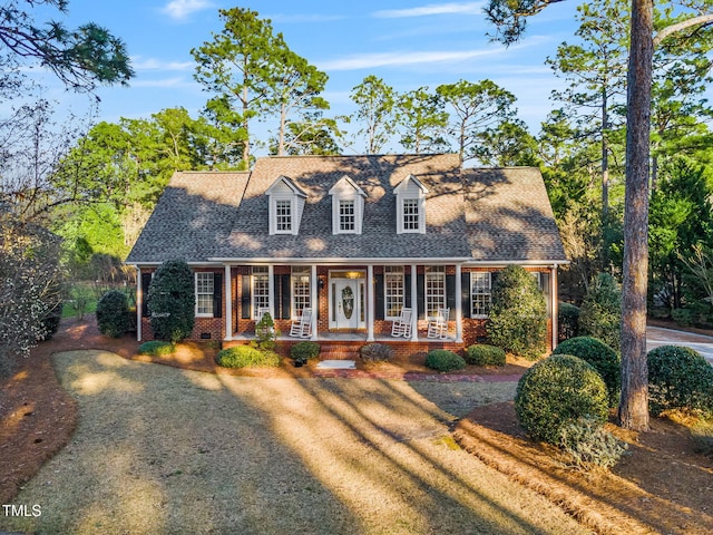 cape cod house with brick siding, covered porch, and a shingled roof