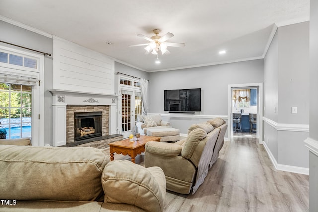 living area with light wood-type flooring, ornamental molding, a fireplace, plenty of natural light, and a ceiling fan