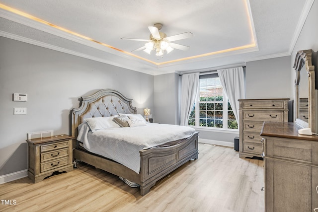 bedroom with a raised ceiling, light wood-style flooring, crown molding, baseboards, and ceiling fan