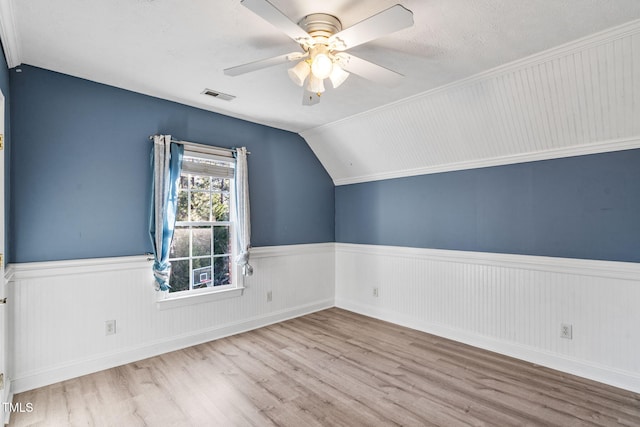 additional living space with wood finished floors, a wainscoted wall, visible vents, lofted ceiling, and ceiling fan