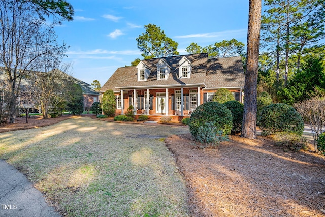 cape cod home featuring brick siding, covered porch, and a front lawn