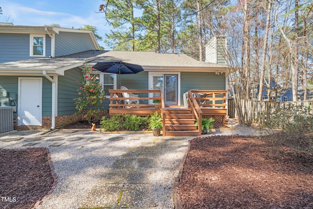 view of front of property featuring central air condition unit, a deck, fence, a shingled roof, and a chimney