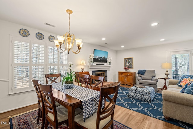 dining room with visible vents, a chandelier, recessed lighting, wood finished floors, and a glass covered fireplace