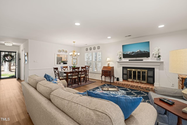 living room with a notable chandelier, recessed lighting, a brick fireplace, and wood finished floors