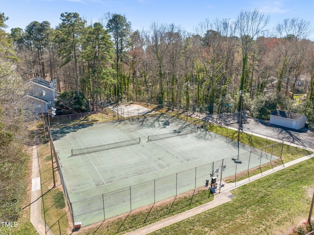 view of tennis court with a forest view, a yard, and fence