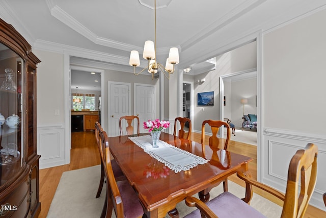 dining space featuring a wainscoted wall, light wood finished floors, ornamental molding, a decorative wall, and a chandelier