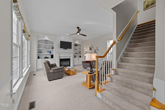 living area featuring a glass covered fireplace, built in shelves, a healthy amount of sunlight, and carpet flooring