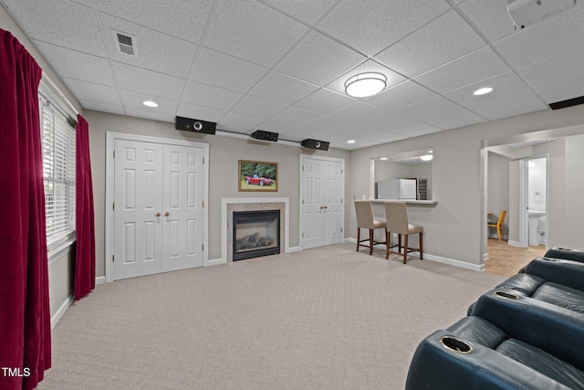 carpeted living area with visible vents, a drop ceiling, recessed lighting, a premium fireplace, and baseboards