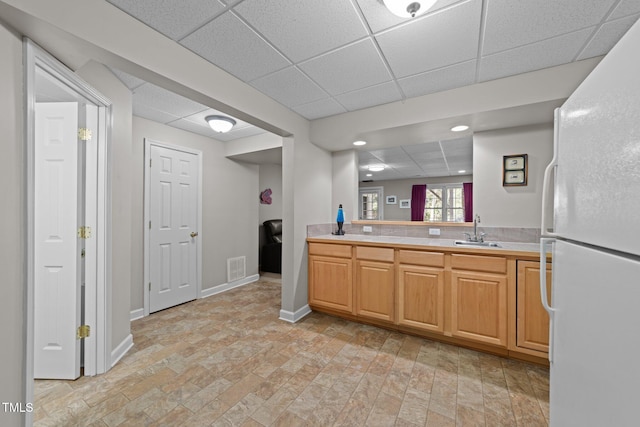 kitchen with baseboards, a drop ceiling, light countertops, freestanding refrigerator, and a sink