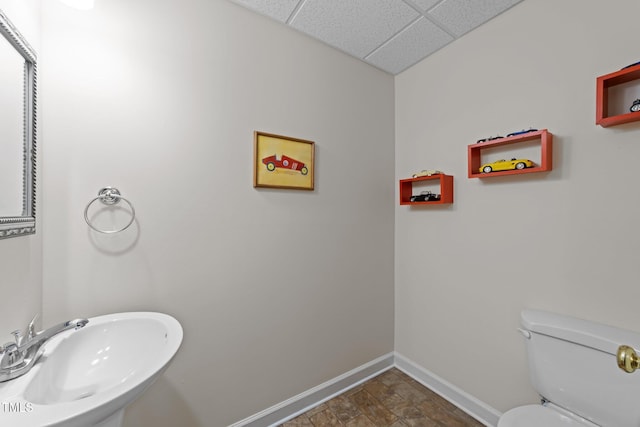 bathroom featuring baseboards, toilet, stone finish floor, a paneled ceiling, and a sink