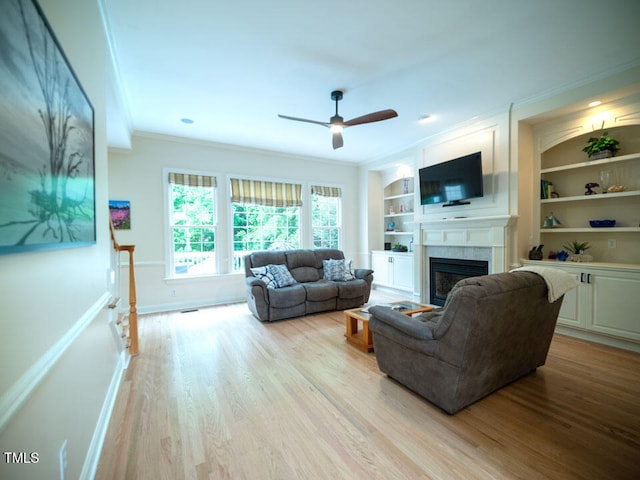 living area featuring ornamental molding, wood finished floors, a fireplace, ceiling fan, and built in shelves