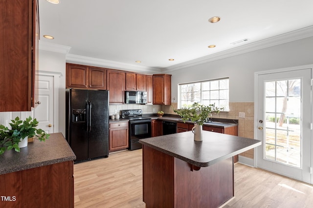 kitchen featuring dark countertops, visible vents, light wood-type flooring, ornamental molding, and black appliances