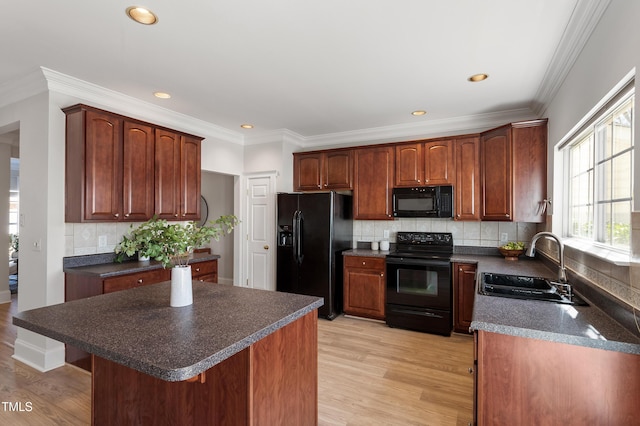 kitchen with dark countertops, crown molding, light wood-type flooring, black appliances, and a sink