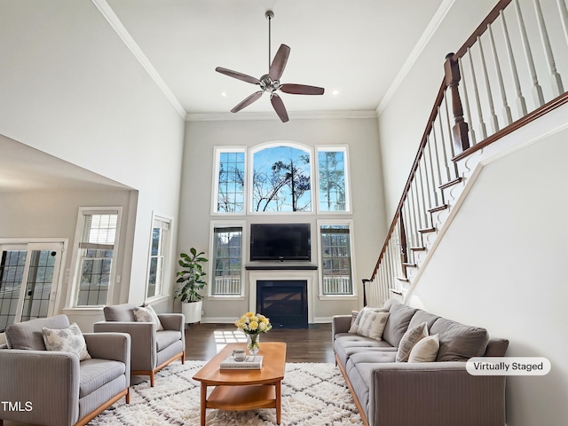 living room with stairs, ornamental molding, a towering ceiling, wood finished floors, and a glass covered fireplace