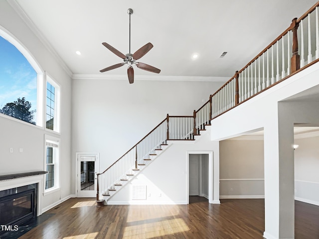 living area featuring crown molding, a fireplace with flush hearth, stairs, a towering ceiling, and wood finished floors