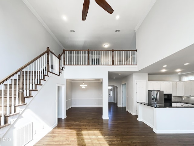 interior space with a ceiling fan, visible vents, baseboards, dark wood finished floors, and crown molding