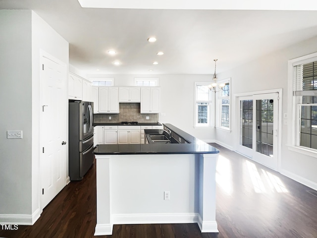 kitchen featuring stainless steel refrigerator with ice dispenser, a sink, dark countertops, white cabinetry, and decorative backsplash