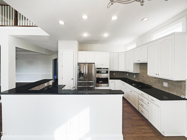 kitchen featuring stainless steel appliances, dark wood-type flooring, white cabinetry, dark countertops, and tasteful backsplash