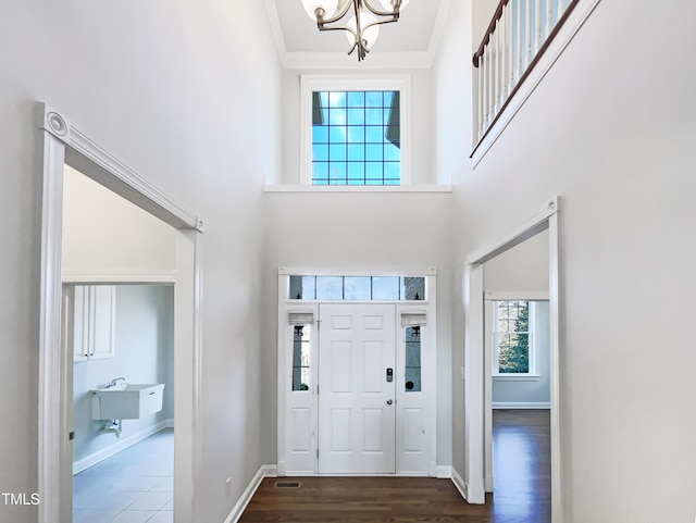 foyer entrance with dark wood-style floors, baseboards, a towering ceiling, and ornamental molding