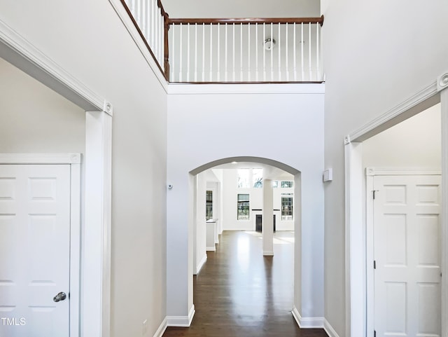 hall featuring dark wood-style floors, arched walkways, baseboards, and a towering ceiling