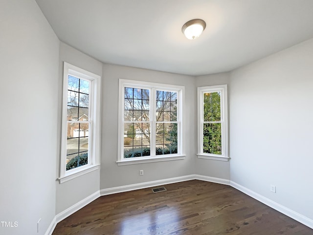 unfurnished room with a healthy amount of sunlight, visible vents, dark wood-style flooring, and baseboards