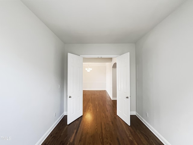 hallway with baseboards, arched walkways, and dark wood finished floors