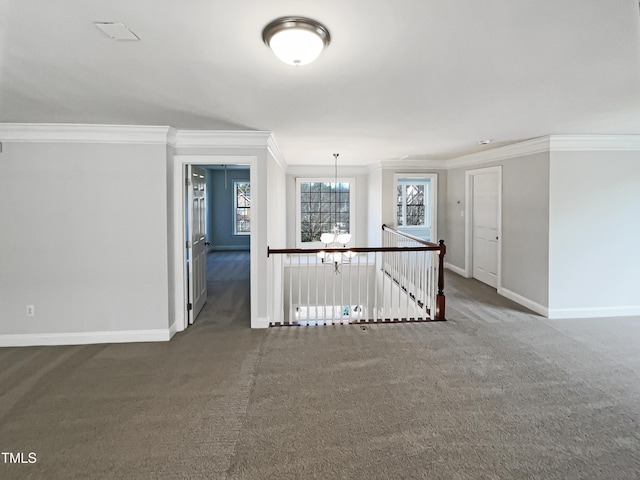 carpeted empty room with a notable chandelier, crown molding, and baseboards